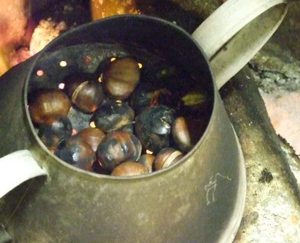 Pormenor de castanhas a assar num recipiente sobre o lume